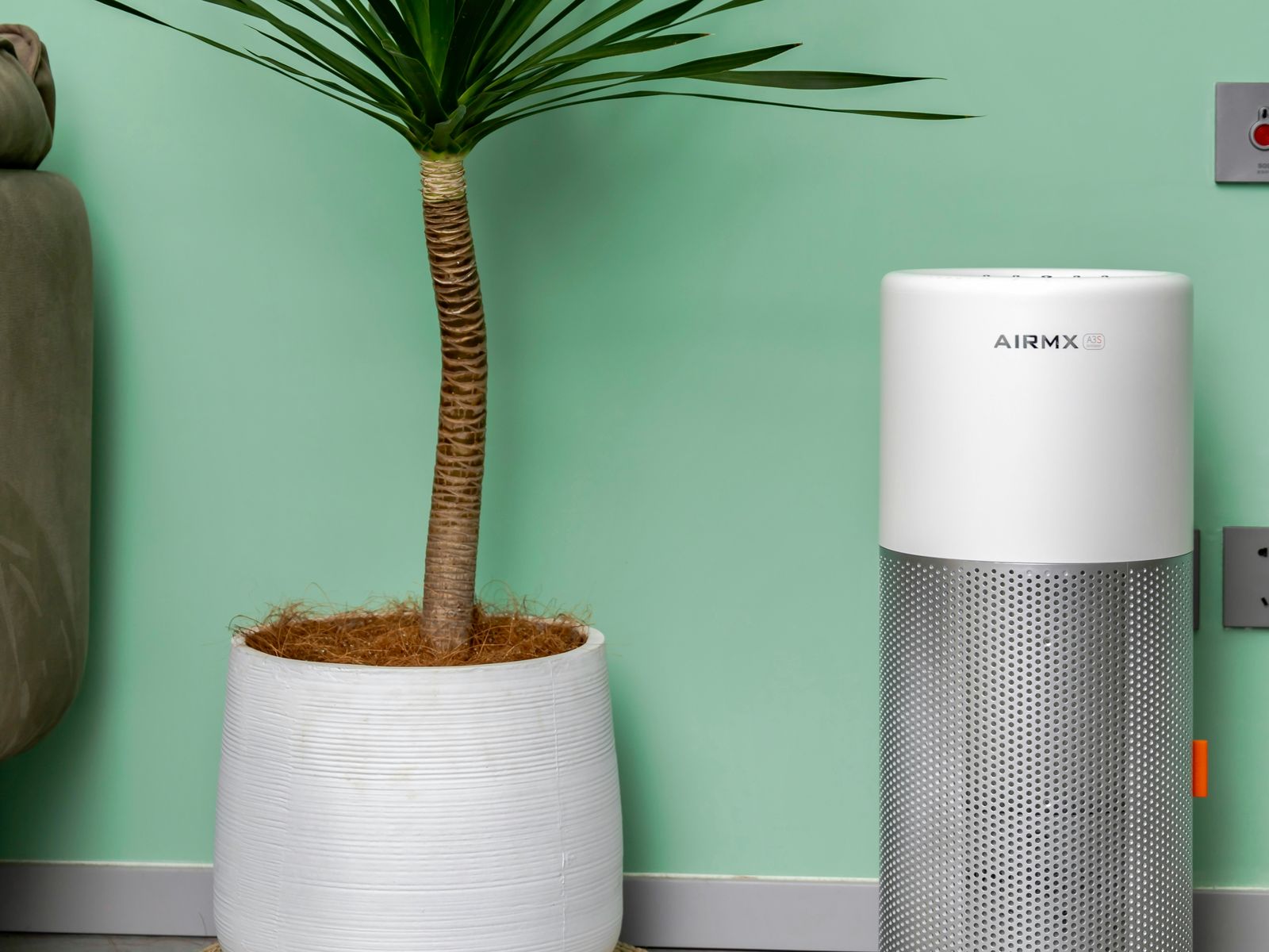 A white-and-silver portable HEPA air purifier standing beside a potted plant in a living room.