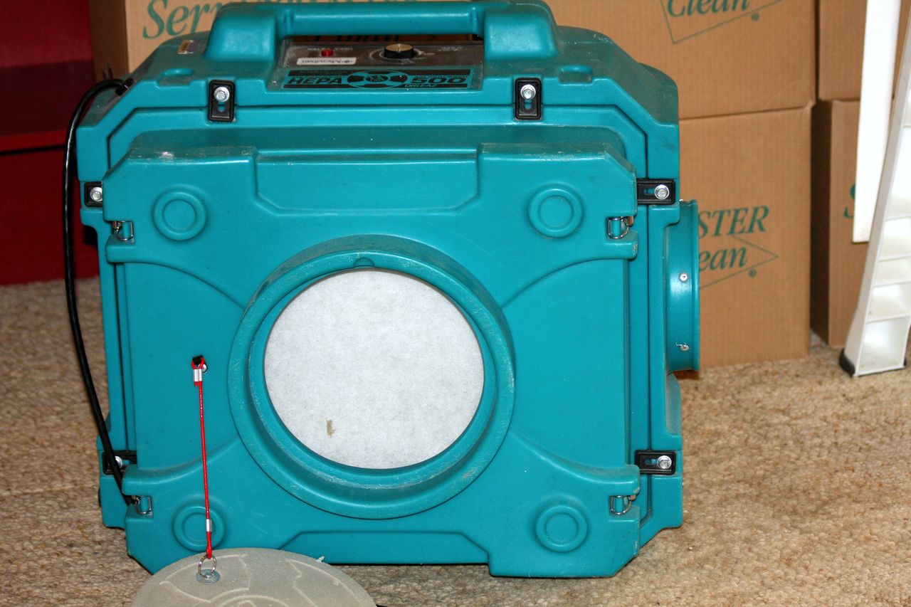 A portable HEPA air scrubber unit on a floor in front of storage boxes