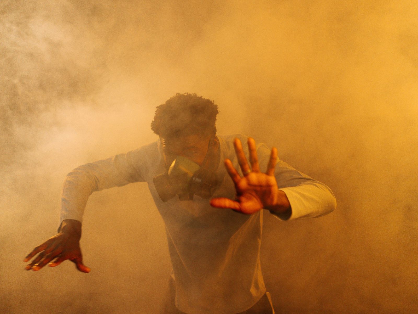 A person wearing a respirator, one hand raised, surrounded by thick orange smoke haze.